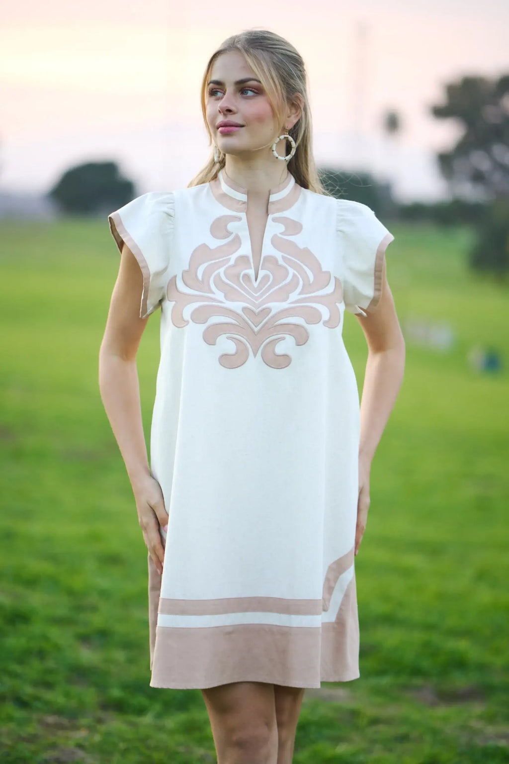 Woman wearing a white dress with beige patterns in an outdoor setting