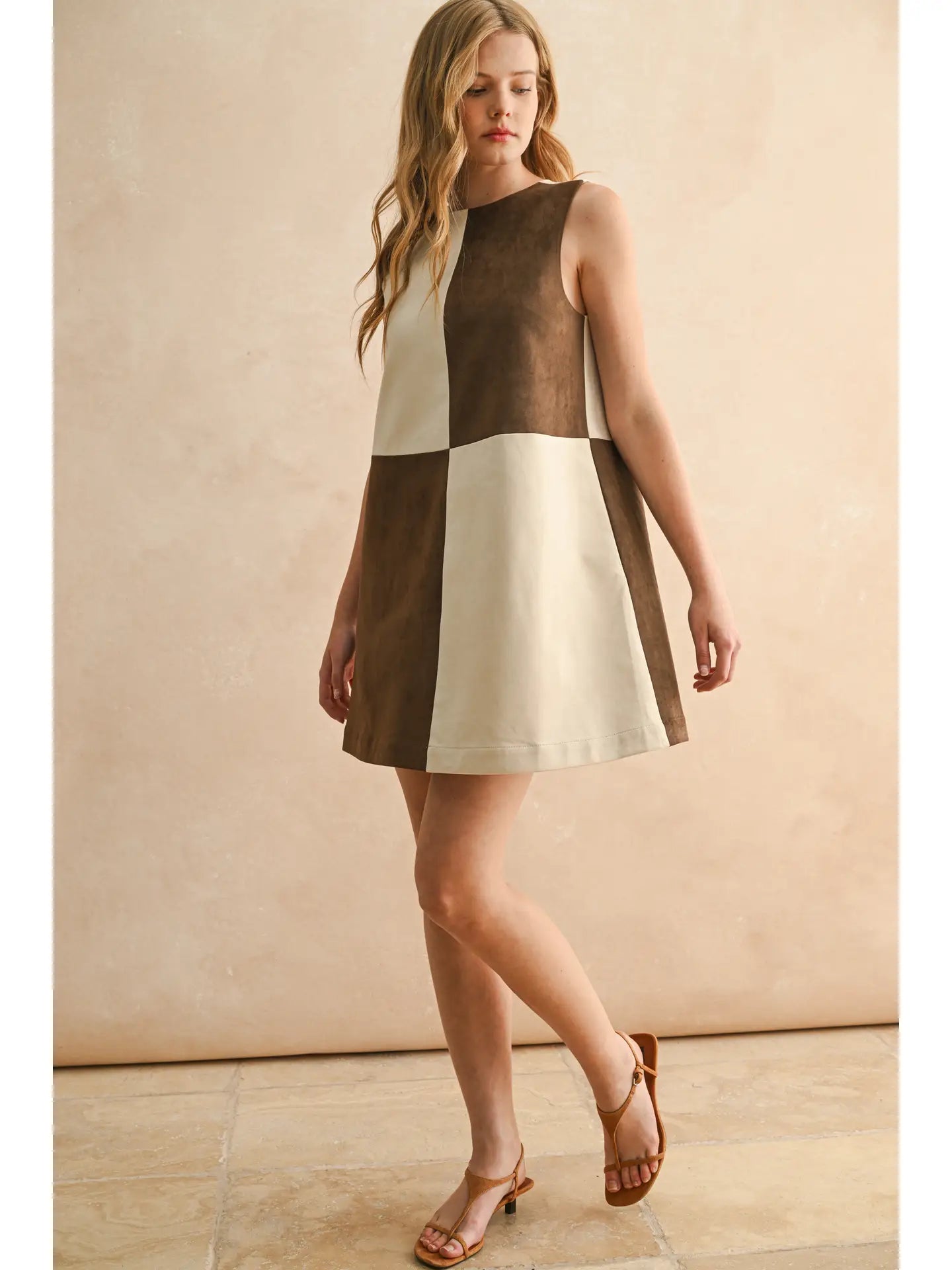 Woman wearing a two-tone dress with a beige and brown color scheme against a neutral background.